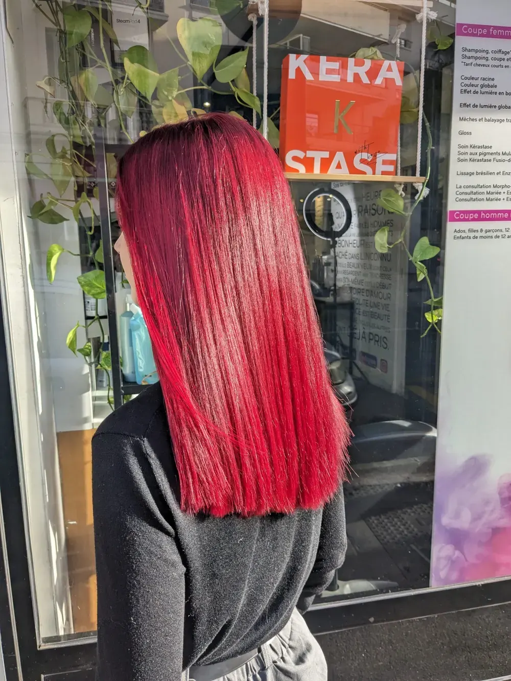 Cherry red colour on straight mid-length hair, seen from behind in front of the salon window