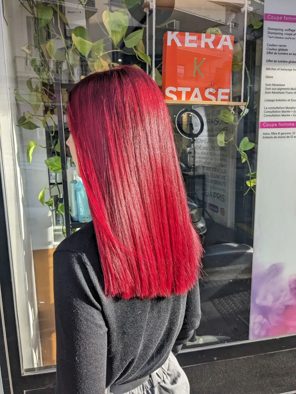 Cherry red colour on straight mid-length hair, seen from behind in front of the salon window
